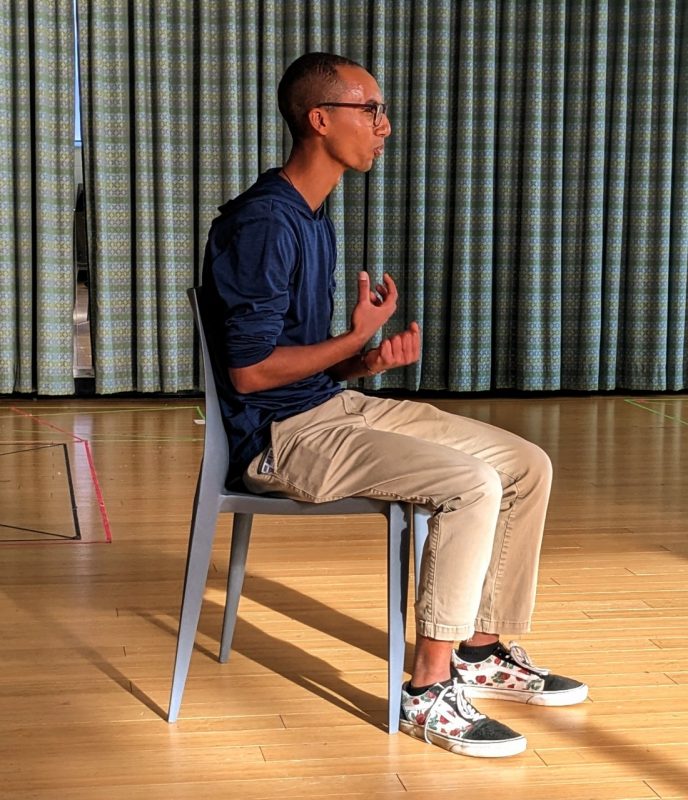A participant sits in a chair, speaking and gesturing with his hands.