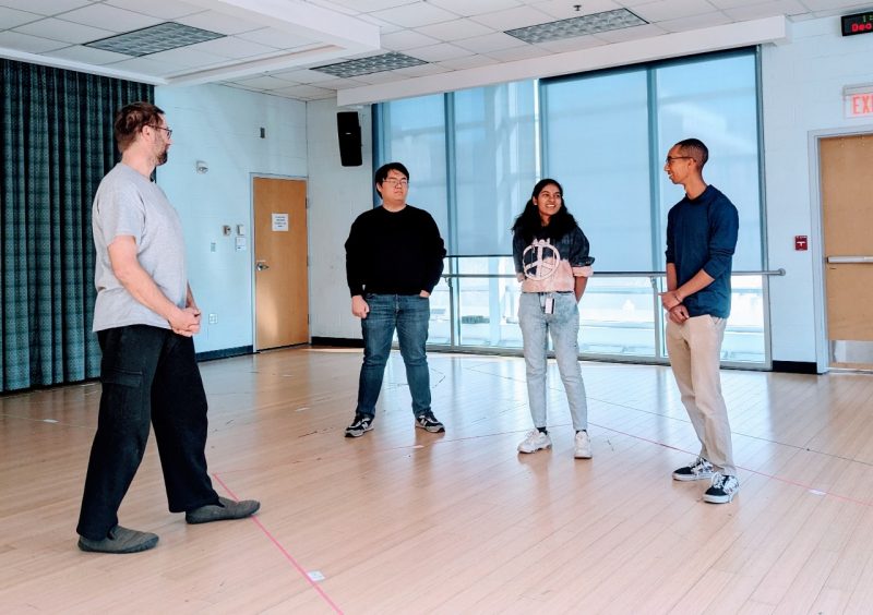 Four participants stand in a semi-circle, looking at each other