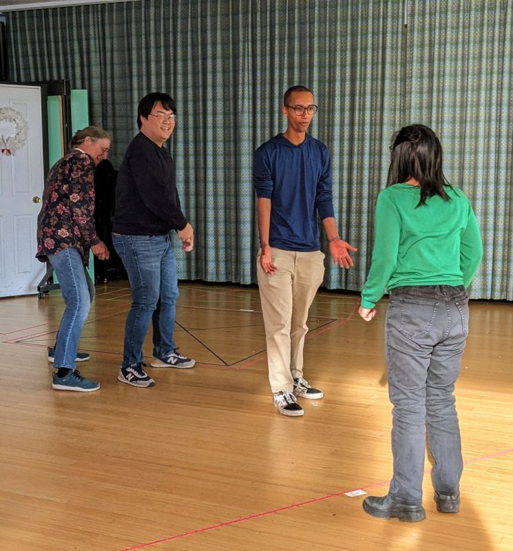 Three participants are in a line facing a fourth. The two participants in the back of the line are miming digging.