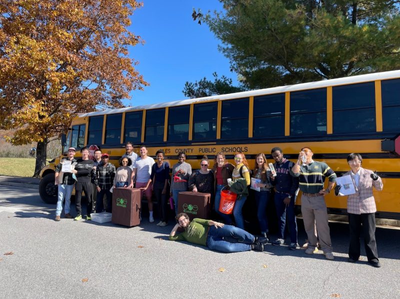 A group of diverse graduate students poses in front of a school bus reading “Giles County Public Schools.”