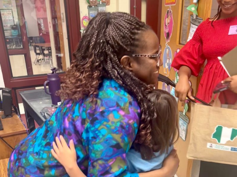 Child hugs smiling woman as another woman looks on smiling as well.