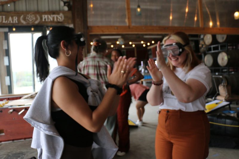 Alexis Mann and a participant play patty-cake with distortion goggles on.