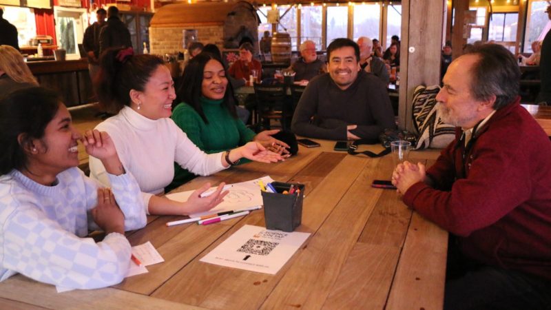 Participants sit and talk around a table, with markers and a piece of paper sitting on the table.