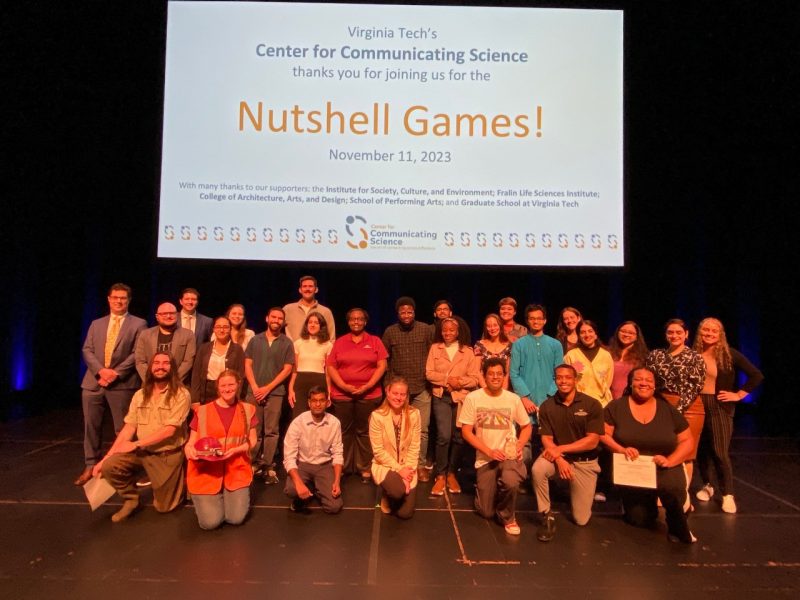 This photo shows 27 people of various genders, races, and national origins posing for a photo beneath a slide that reads "Virginia Tech's Center for Communicating Science thanks you for joining us for the Nutshell Games!"