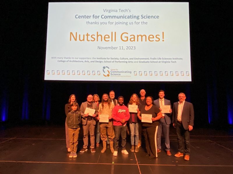 This photo shows the five winners and seven judges for the Nutshell Games,  people of various genders, races, and national origins, posing for a photo beneath a slide that reads "Virginia Tech's Center for Communicating Science thanks you for joining us for the Nutshell Games!"