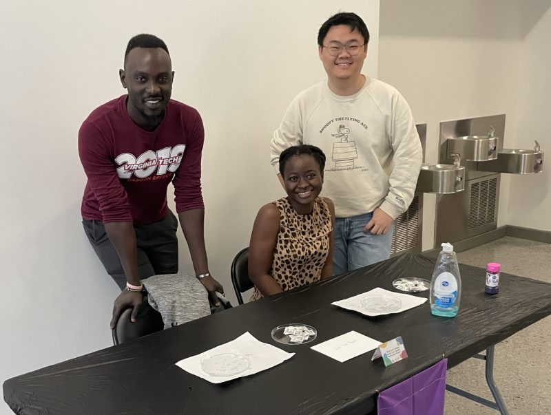 Ama Essuman Hokie for a Day with Ivan Odur and Ying-Xian Goh A photo of a young women sitting in the middle of two standing men.