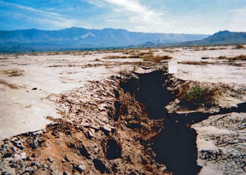fissures A picture of a ground fissure in a desert with mountains and a blue sky in the background.
