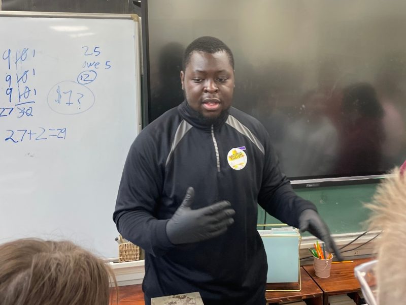 Nana_Siaw-Mensah_3 A graduate student stands in front of the classroom mid-gesture while explaining his research to curious students.
