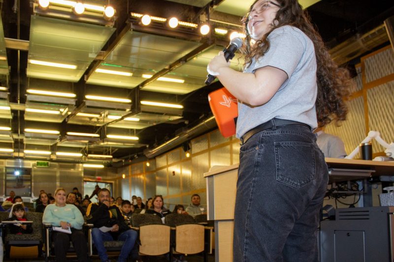 Mariana stands in front of an energy crowd with a microphone in hand as she gives a presentation.