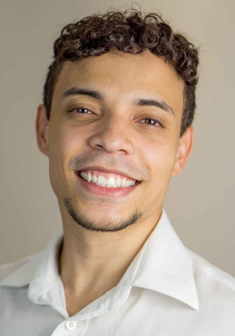 Headhot of a young male PhD student with a white colored button up dress shirt and a smile. 