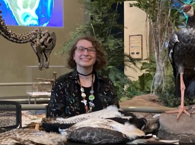 Jay Margolis running a museum event booth with bird taxidermy and a duck-billed dinosaur display in the background. Birds are the only living group of dinosaurs, so evolutionary bird research often overlaps with paleontology. Photo courtesy of Lindsay Kastroll.