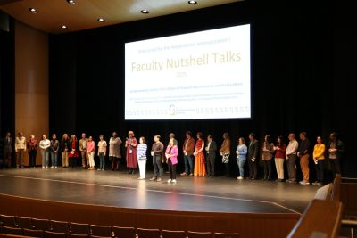Participants, judges, and the three prize-winning presenters celebrate the Faculty Nutshell Talks on stage as the audience cheers.