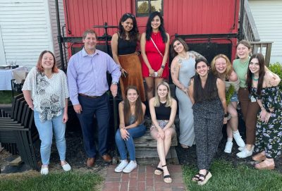 A smiling group of graduate students and their advisor, posing for a picture in front of a caboose.
