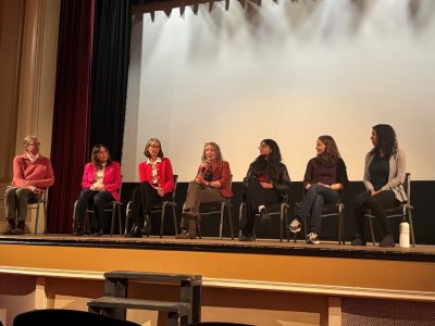 This photo shows seven women seated on a stage.