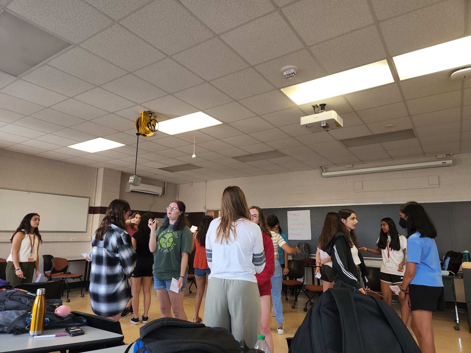 Students gather in a classroom environment. Most are talking in pairs.