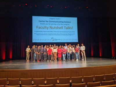 This photo shows a stage and a group of a couple dozen people posing for a photo. Behind them is a large slide reading "Virginia Tech's Center for Communicating Science thanks you for joining us for the inaugural Faculty Nutshell Talks!"