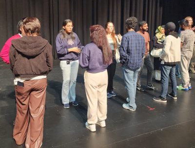 This photo shows two lines of young people of a variety of races and ethnicities talking in partnerships. Ten people are clearly visible, with a couple more at the far end of the line partially visible.