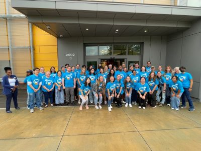 This photo shows a large groups of people (40-50) dressed in matching blue t-shirts and posing for a photo.