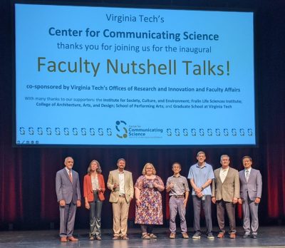 This photo shows a group of  8 people standing on a stage and posing for the camera. Behind and above them is a large slide reading "Virginia Tech's Center for Communicating Science thanks you for joining us for the inaugural Faculty Nutshell Talks!"