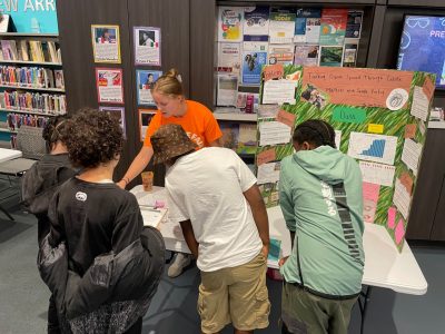 This photo shows a Flip the Fair researcher presenting to four 5th graders.