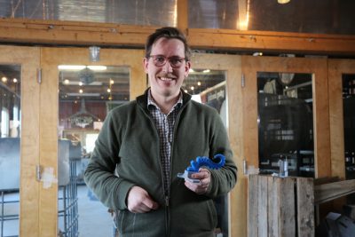 Naughton holds an octopus arm prototype and smiles to the camera.